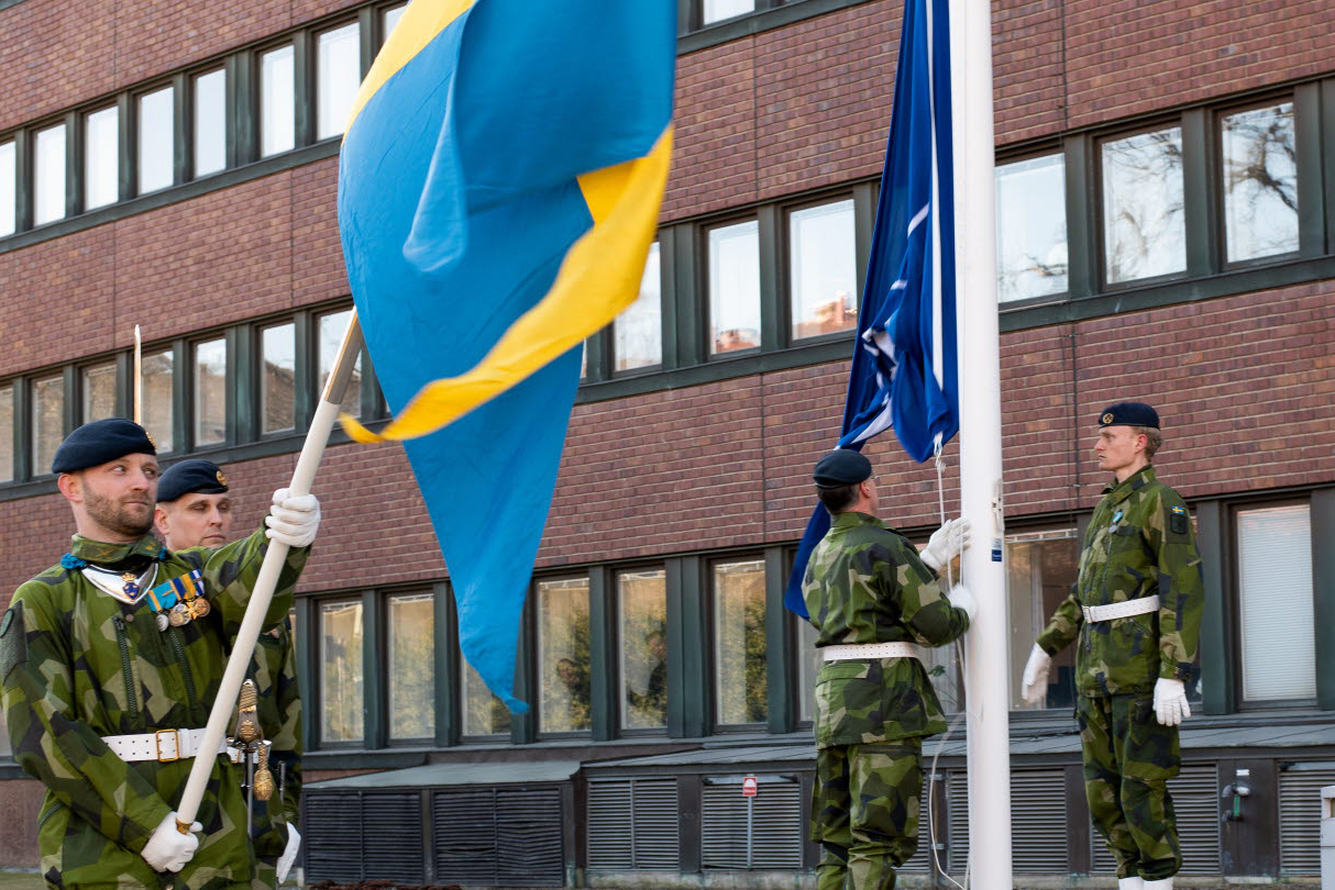 Soldiers raising a NATO flag and a Swedish flag.