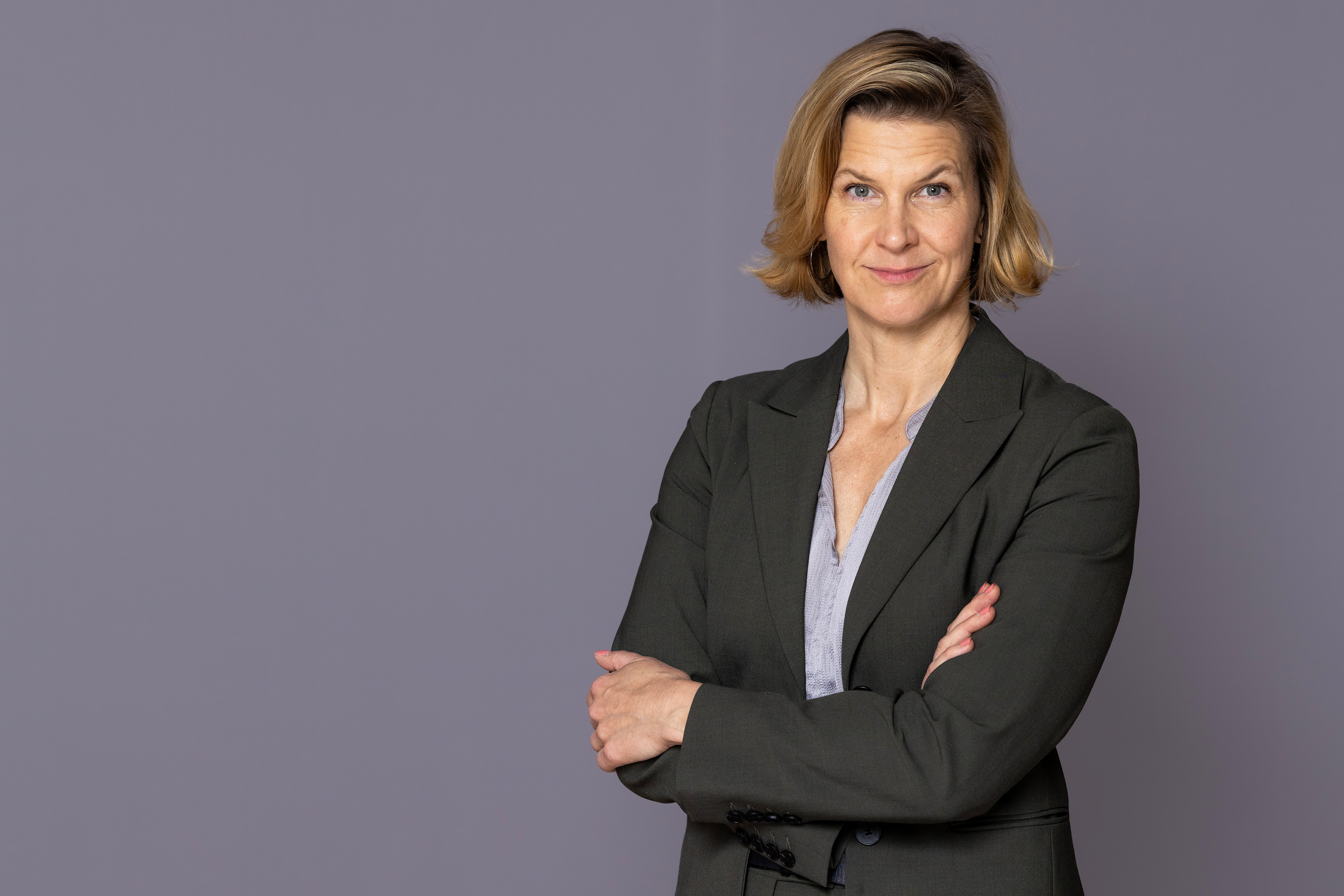 Minister for Gender Equality Nina Larsson stands in front of a gray wall and looks into the camera.