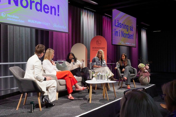 People sitting in chairs and a sofa having a conversation on a stage.