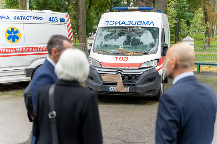 An ambulace with its window crushed. The Minister for Health Care Acko Ankarberg Johansson iss sen in the foreground, looking at the ambulance.